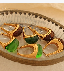 Close-up of vintage U-shaped earrings with green and amber stones on glass tray