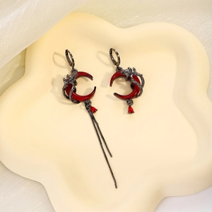 Gothic asymmetrical dragon and red moon earrings with long tassels on a cream tray
