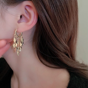 Close-up of golden metal tassel earrings with layered wheat leaf design on a female model