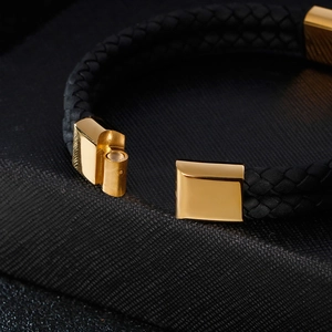 Detailed close-up of the golden magnetic steel clasp on a black braided leather bracelet