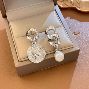 Detailed shot of asymmetric silver coin earring and white pearl drop on leather padding