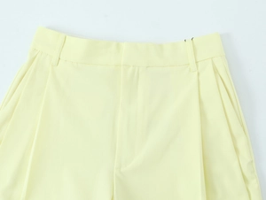Details einer hellgelben Hose mit Gürtelschlaufen und präzisen Falten auf glattem Stoff