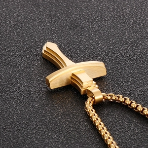 Vue macro du pendentif croix dorée en acier inoxydable brossé avec chaîne box