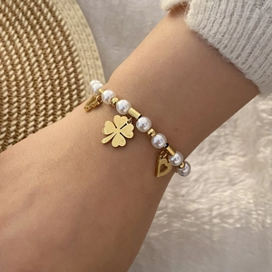 Handgefertigtes Perlenarmband mit goldenem Kleeblatt- und Herzanhänger auf Strickhintergrund