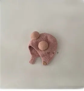 Detailed texture of pink plush baby earflap hat with brown pom-poms and wood button