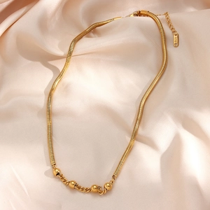 Minimalist gold snake chain necklace with four polished beads on silk fabric