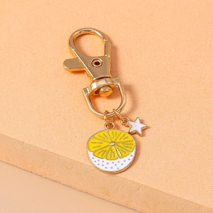 Detailed close-up of a yellow lemon slice and white star enamel charms on a gold keychain