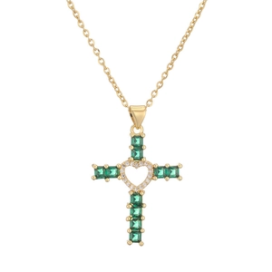 Macro detail of gold cross pendant with emerald green stones and heart-shaped center