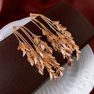 Macro shot of gold-plated leaf tassel earrings on elegant brown leather display
