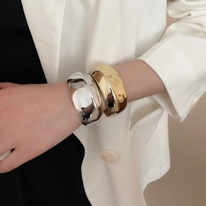Bracciali rigidi irregolari in metallo lucido oro e argento indossati da una modella
