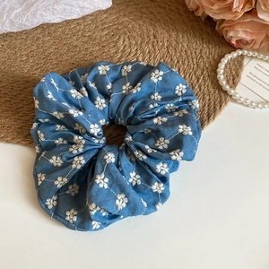 Detail of blue denim scrunchie with white daisy embroidery on a soft fabric texture