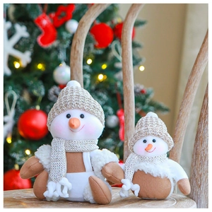 Close-up of two knit plush snowmen with carrot noses and beige scarves on wood