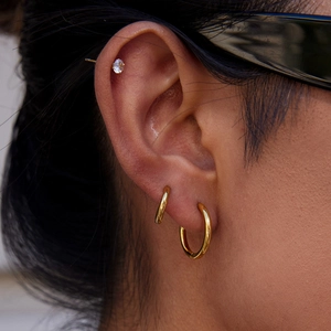Boucles d'oreilles créoles dorées en acier inoxydable et clous portés par un mannequin