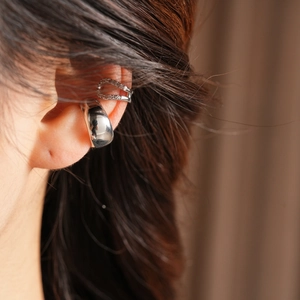 Detail view of two silver zircon-encrusted ear cuffs worn on model's ear cartilage