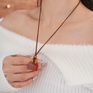 Detail of red faux stone bag pendant with wooden bead on brown leather necklace