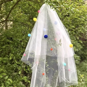 Detail of white double-layer mesh veil decorated with colorful pom-poms hanging on a tree