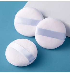 Detailed view of three soft white plush powder puffs with light blue satin ribbon handles