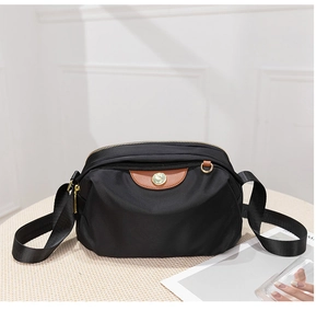 Detailed view of black oxford crossbody bag with brown leather trim and gold hardware