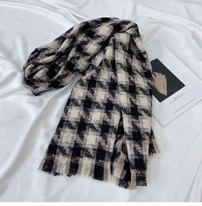 Close-up of thick houndstooth scarf with tassels on white soft fabric background