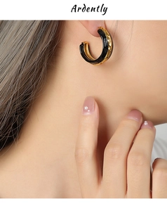 Close-up of C-shaped gold-plated hoop earrings with black enamel and wavy texture
