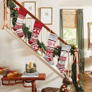 Knitted Christmas stockings with reindeer and snowflake patterns hanging on staircase railing