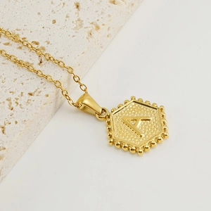 Detail of gold hexagon pendant featuring embossed letter A with beaded edge on chain