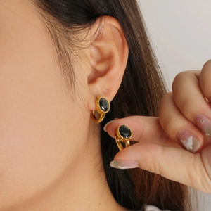 Detailed close-up of golden huggie earrings featuring oval black zircon and beaded setting