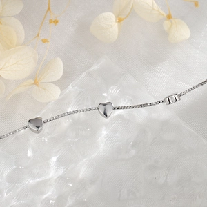 Detailed view of silver heart bracelet with box chain on a glass base background