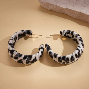 Detailed view of C-shaped leopard print earrings with gold pins on stone background
