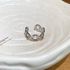 Macro shot of silver adjustable open ring with hollow smiley faces on a ceramic tray