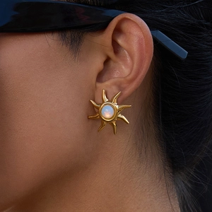 Nahaufnahme von goldenen Sonnenohrringen mit Regenbogen-Opal auf einem Model mit Brille