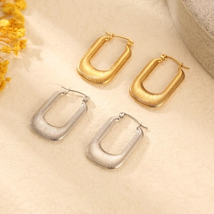 Minimalist square U-shaped gold and silver earrings with stripe texture on beige fabric