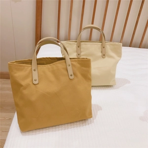 Detail of solid color canvas tote bags with reinforced leather handles and metal rivets