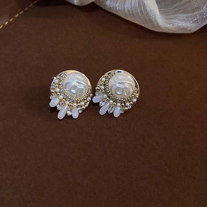 Detail of gold earrings featuring shell texture, white baroque pearls, and crystal fringes