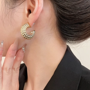 Close-up of golden C-shaped hoop earrings with textured granular scale pattern