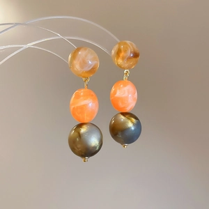 Close-up of three-tier amber and orange resin bead earrings with golden metal accents