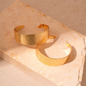 Détail de boucles d'oreilles créoles dorées en C avec texture en métal brossé sur pierre