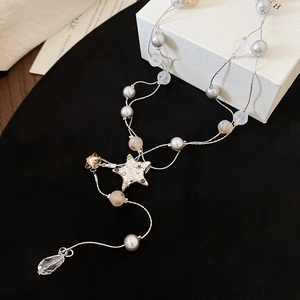 Macro detail of a double-layer pearl necklace with a star charm and crystal teardrop pendant