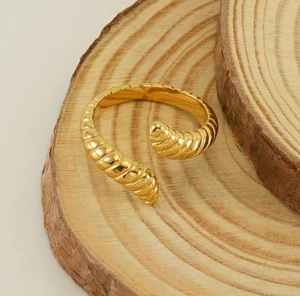 Detailed view of a gold croissant ring with polished spiral texture on a wood base