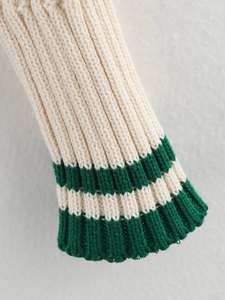 Close-up of cream knit sweater cuff with dark green stripes and ribbed texture