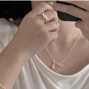 Macro view of minimalist silver knot ring and dainty pearl bow necklace set