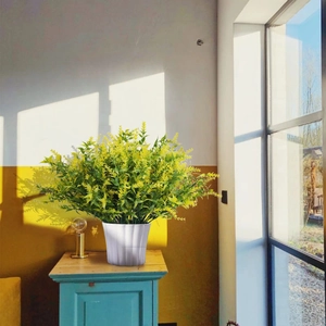 Artificial yellow lavender potted plant on a teal wooden table with soft sunlight