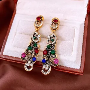 Vintage gold peacock dangle earrings with colorful rhinestones on a leather box