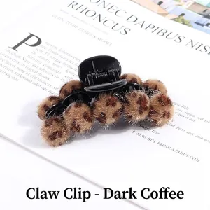Close-up of plush leopard print faux fur pom poms on a dark coffee brown hair banana clip