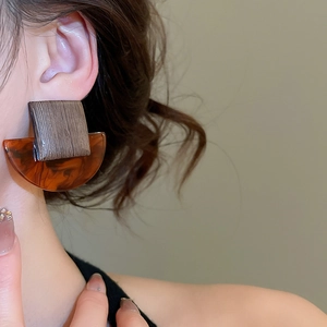 Detail of square wood and amber resin geometric stud earrings worn on a model's ear