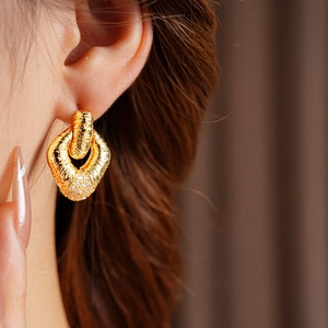 Close-up of gold diamond-studded woven texture earrings worn by a model
