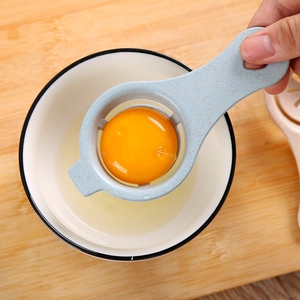 Mini wheat straw egg separator in light blue isolating yolk over a bowl on wooden board