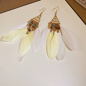Detail of bohemian long white feather earrings with gold geometric pendants and beads