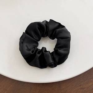 Detail of a shiny black satin scrunchie placed on a white plate with wooden background