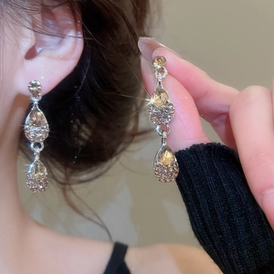Detailed view of elegant drop-shaped champagne crystal earrings on a model’s ear